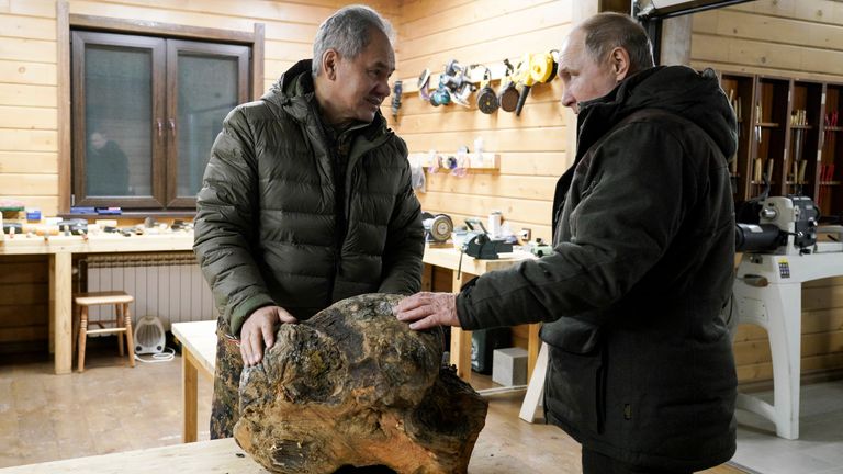 Russia Defense Minister Sergei Shoigu, left, and Russian President Vladimir Putin talk to each other and look at a piece of wood for crafting at Sergei Shoigu's workroom in a taiga forest in Russia's Siberian region in Russia. 